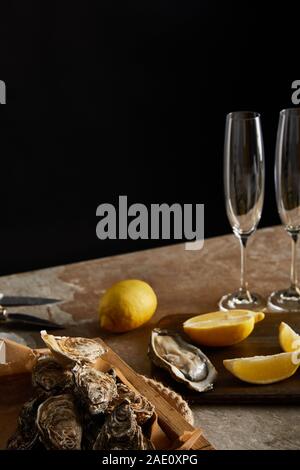 selective focus of oysters in shells near lemons on wooden cutting board and champagne glasses isolated on black Stock Photo