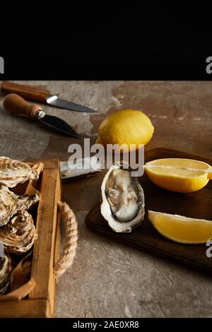 selective focus of delicious oysters near lemons and knifes isolated on black Stock Photo