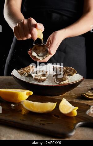 selective focus of woman squeezing lemon on oyster isolated on black Stock Photo