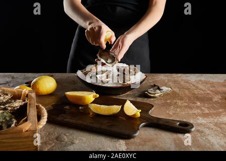 cropped view of woman squeezing lemon on oyster isolated on black Stock Photo