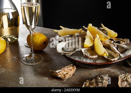 selective focus of oysters and lemons in bowl with ice near sparkling wine in champagne glass isolated on black Stock Photo