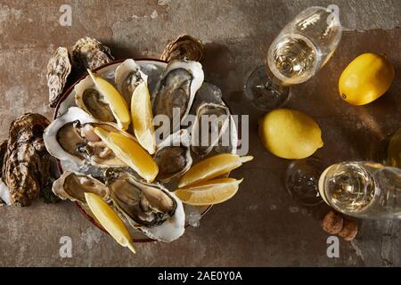 top view of delicious oysters and lemons in bowl near champagne glasses with sparkling wine Stock Photo