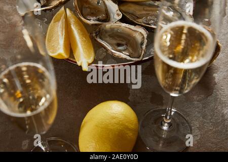 selective focus of oysters and lemons in bowl with ice near champagne glasses with sparkling wine Stock Photo