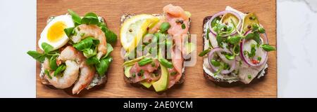 panoramic shot of wooden cutting board with smorrebrod sandwiches on white marble surface Stock Photo