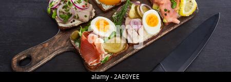 panoramic shot of wooden cutting board with danish smorrebrod sandwiches near knife on grey surface Stock Photo