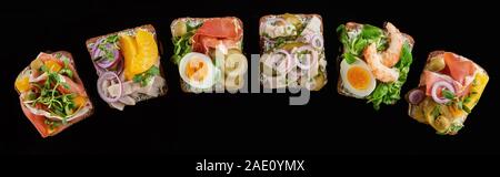 panoramic shot of rye bread with prepared danish smorrebrod sandwiches isolated on black Stock Photo