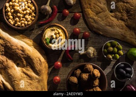 top view of delicious falafel, hummus, chickpeas, pita, vegetables and olives on wooden rustic table Stock Photo