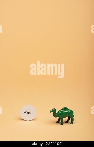 Green toy camel with lettering water on card on yellow background, water scarcity concept Stock Photo