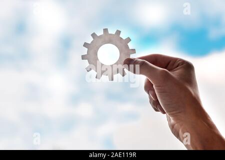 cropped view of man holding gears on blue sky background Stock Photo