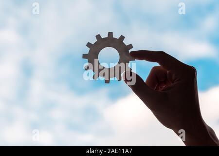 cropped view of man holding gears on blue sky background Stock Photo