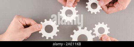 cropped view of people holding white gears on grey background, panoramic shot Stock Photo