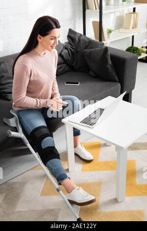 attractive woman with broken leg having online consultation with doctor on laptop at home Stock Photo