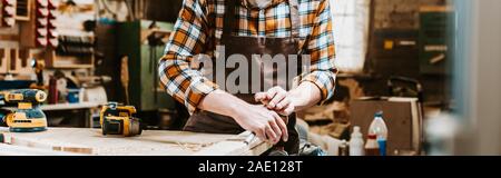 panoramic shot of woodworker holding chisel while carving wood in workshop Stock Photo