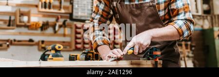 panoramic shot of carpenter holding chisel while carving wood in workshop Stock Photo