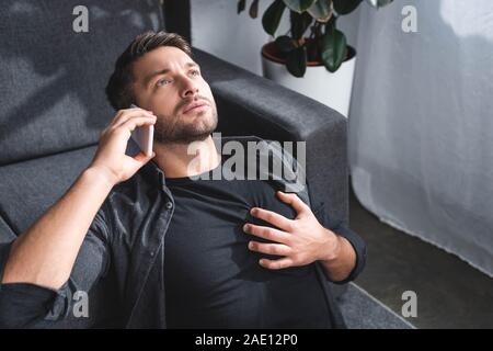 high angle view of handsome man having heart attack and talking on smartphone in apartment Stock Photo