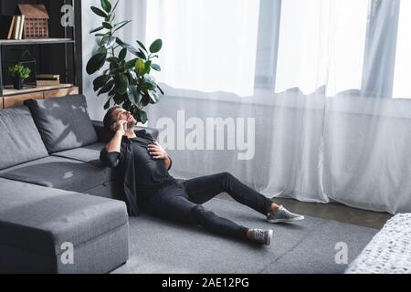 high angle view of handsome man having heart attack and talking on smartphone in apartment Stock Photo