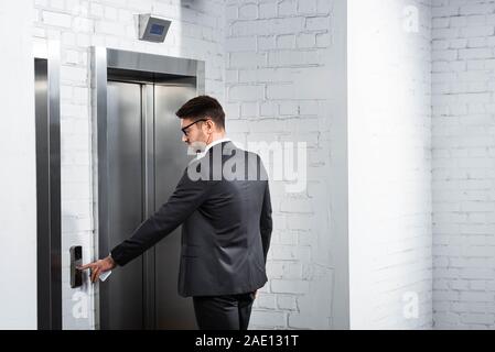 businessman in suit pushing button of elevator in office Stock Photo