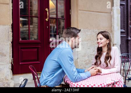 happy young couple holding hands and looking at each other while sitting in street cafe Stock Photo