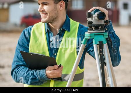 Smiling surveyor holding clipboard and digital level Stock Photo