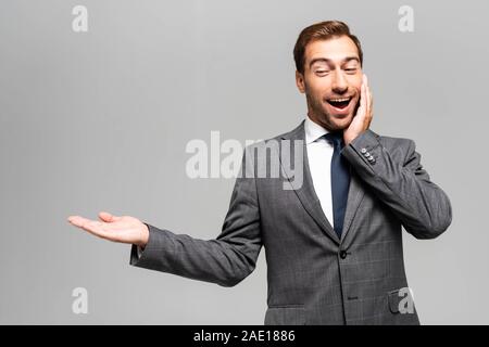 handsome and shocked businessman in suit pointing with hand isolated on grey Stock Photo
