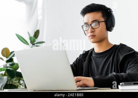 asian hacker in headphones using laptop and sitting at table Stock Photo