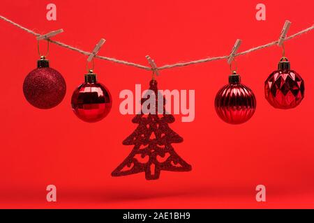New Year Christmas background. Red Christmas toys balls on a string with clothespins on a red background, preparing for the new year and Christmas. Stock Photo