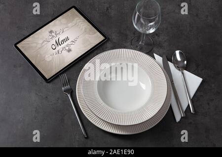 Tablet with stylish restaurant logo and laid table Stock Photo