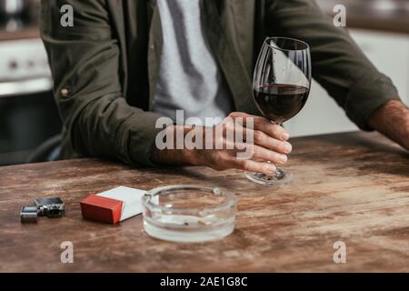 Cropped view of man holding wine glass with cigarettes and ashtray on table Stock Photo