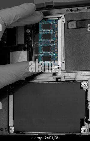 Technician installing RAM into the memory slot on a laptop computer.  Abstract image with selective colour Stock Photo
