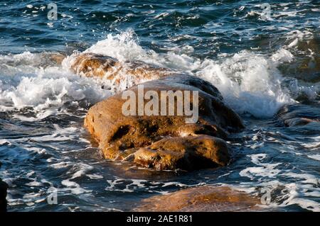 Sydney Australia, wave in the harbour breaking over rocks in late afternoon sun Stock Photo