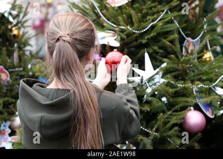 Girl decorates Christmas tree on a street, toy balls on fir branches. Concept of New Year celebration, winter holiday Stock Photo