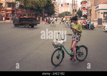 Chengdu, China -  July 2019 : Woman on a bicycle standing on a road and checking her mobile phone in the city of Chengdu in summer, Sichuan Province Stock Photo