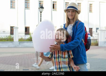 Happy kids, brother and sister holding cotton candy on the street in sunny day Stock Photo
