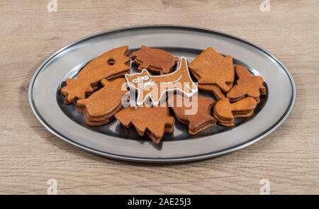 Cute white decorated gingerbread cat. Mix of stacked varied shaped cookies on shiny plate. Sweet Christmas candies in round platter on wood background. Stock Photo