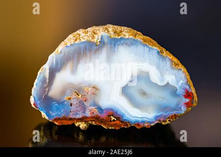 White blue polished agate gem cross-section. Reflection on colored background. One quartz chalcedony detail. Crystals in a small geode. Ice like look.