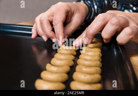 Female hands placing vanilla crescent roll cookies dough on black baking tray. Shaping traditional Czech Christmas and wedding nutty sweets. Sheet pan. Stock Photo