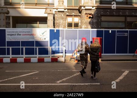 Two ladies in winter coats cross road towards construction site Stock Photo