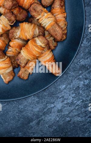 Vegan pigs in blankets in a tray on a slate background. Cooked morrisons no pigs in blankets. Plant based meat free alternative Stock Photo