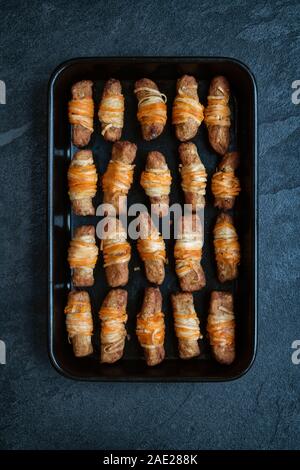 Vegan pigs in blankets in a tray on a slate background. Cooked morrisons no pigs in blankets. Plant based meat free alternative Stock Photo