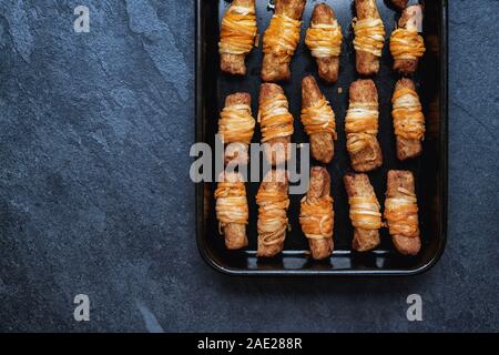 Vegan pigs in blankets in a tray on a slate background. Cooked morrisons no pigs in blankets. Plant based meat free alternative Stock Photo