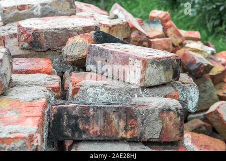 Stacks of old red broken dirty burnt bricks with remnants of cement on grass in garden. Stock Photo