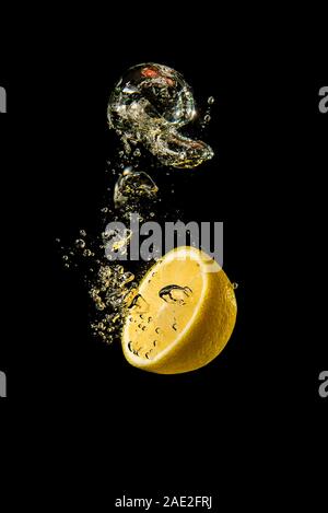 Fresh yellow lemon half in water splash on black background with lots of air bubbles. Stock Photo