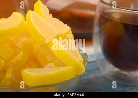 Marmalade lemon slices, a glass of black tea and a teapot with brewed tea on a wooden background. Sweet dessert. Close up Stock Photo