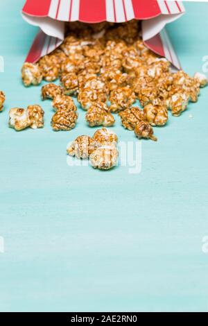 Popcorn on turquoise background. Caramel pocorm in the red and white cup. Cinema. Movie time. Stock Photo