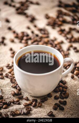 A cup of strong black coffee and scattered grains on the burlap. Fragrant invigorating drink from freshly roasted coffee beans Stock Photo