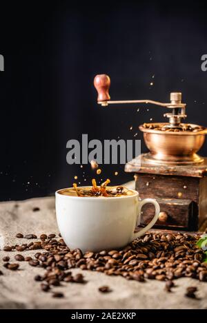 A Cup of coffee with frozen splashes in the air and a wooden vintage coffee grinder. Fragrant invigorating drink from freshly roasted coffee beans. Stock Photo