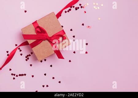 Gift box decorated with red bow on pink background with heart shape glitter confetti. Stock Photo