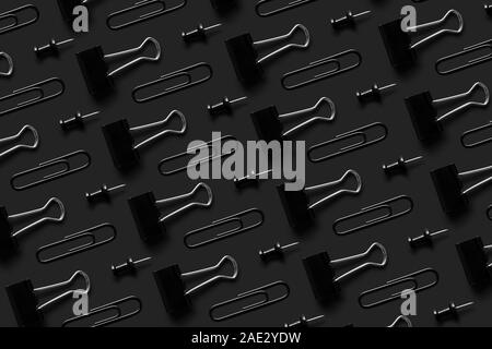 Black office supplies, paper clips, pushpin and binder clips organized neatly over black background, top view Stock Photo