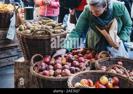 London, UK - November 29, 2019: Woman buying fresh apples from Teds Veg stall in Borough Market, one of the largest and oldest food markets in London. Stock Photo