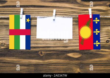 Hanging flags of Central African Republic and Guadeloupe attached to rope with clothes pins with copy space on white note paper on wooden background.D Stock Photo